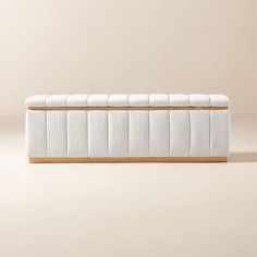 a white upholstered bench with wooden legs on a beige background in front of a wall