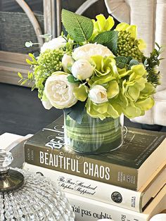 a vase filled with white and green flowers on top of two books next to a candle