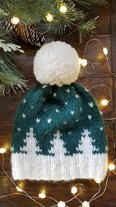 a green and white knitted hat sitting on top of a wooden table next to christmas lights