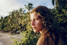 a woman standing on the beach with her hair blowing in the wind and palm trees behind her