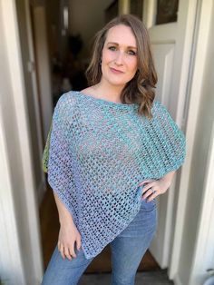 a woman standing in front of a door wearing a blue crocheted ponchy