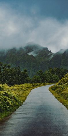 an empty road with mountains in the distance and clouds rolling over it on a cloudy day