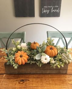 a basket filled with pumpkins and greenery on top of a wooden table