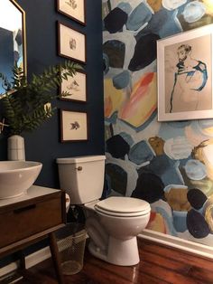 a white toilet sitting in a bathroom next to a sink and painting on the wall