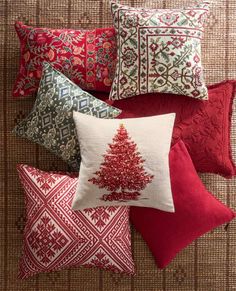 red and green pillows with embroidered christmas tree on them, sitting on a woven surface