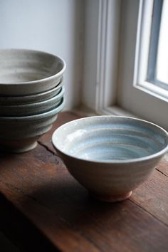 a stack of white bowls sitting on top of a wooden table next to a window