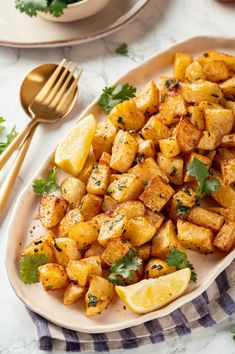 a white plate topped with potatoes and lemon wedges next to a bowl of parsley