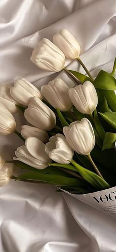 a bouquet of white tulips laying on top of a white bed sheet with the word voda written in it