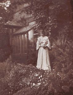 an old photo of a woman standing in front of a house surrounded by greenery