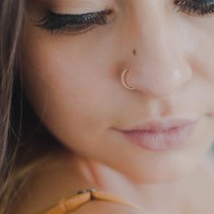 a close up of a woman with her eyes closed wearing a nose ring and piercing