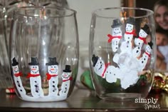 two glasses with snowmen painted on them sitting on a table next to a christmas ornament