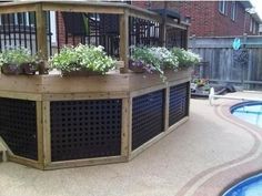 a deck with flowers and plants on it next to a swimming pool in a backyard