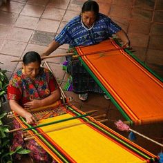 two women working on weavings in an outdoor area with plants and potted plants