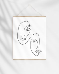 two faces drawn in one line on a white wall with a wooden frame hanging from the wall