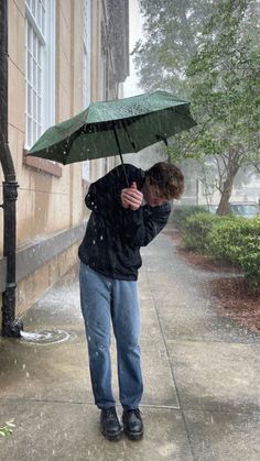 a man is standing under an umbrella on the sidewalk in the rain while it's raining