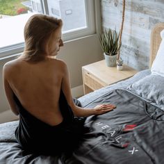 a woman sitting on top of a bed in front of a window next to a plant