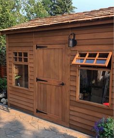 a small wooden shed with windows on the side and a brick walkway leading up to it