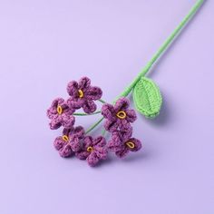 crocheted purple flowers with green leaves on a light purple background, closeup