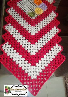 a red and white crocheted table runner with flowers on the edge, sitting on a tile floor