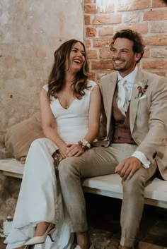 a man and woman sitting next to each other on a bench in front of a brick wall