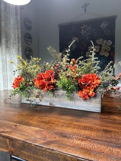 an arrangement of flowers in a wooden box on top of a wood table next to a mirror