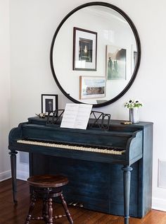 a black piano sitting on top of a hard wood floor next to a round mirror