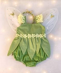 a green fairy romper with white flowers on the side and wings attached to it