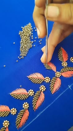 a person is working on some beading with scissors and thread in front of a blue table