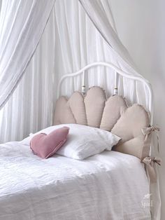 a white bed with a pink pillow on it's headboard and canopy over it