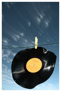 an old vinyl record hanging on a clothes line under a blue sky with wispy clouds