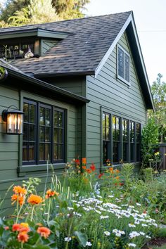 a green house with lots of flowers in the front yard and side walk leading up to it