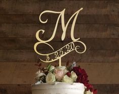 a wedding cake with the letter m on it and flowers in front of wooden background