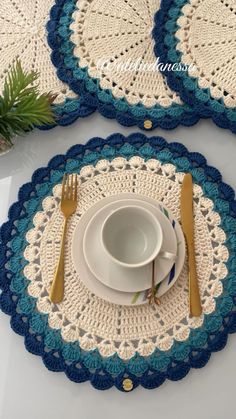 two crocheted placemats on top of each other with gold forks and spoons