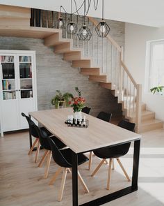 a wooden table with black chairs under a stair case