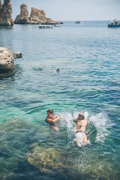 two people swimming in the ocean near rocks