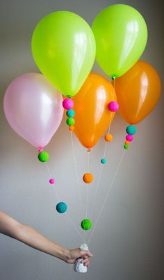 a bunch of balloons that are being held by someone's hand in front of a wall