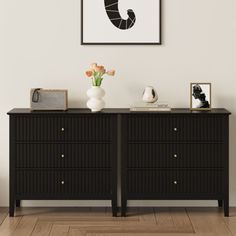 a black dresser with flowers and pictures on the wall above it in a white room