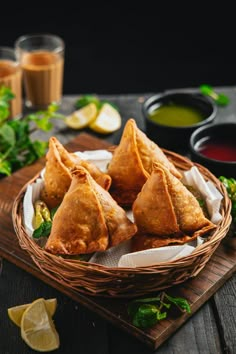 some food that is in a basket on a wooden table with lemon wedges and dipping sauce