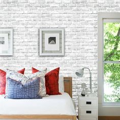 a bedroom with white brick walls, red and blue pillows and pictures on the wall