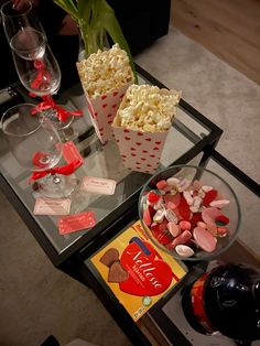 a glass table topped with two cups filled with candy and popcorn next to wine glasses