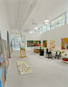 an artist's studio with paintings and easels on the wall, in front of windows