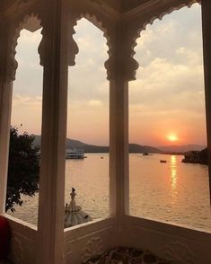 the sun is setting over the water from an ornate window in a room with large windows