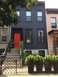 two story house with red door and black fenced in area next to the stairs