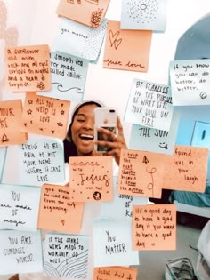 a woman holding a cell phone in front of a wall covered with notes and post it notes