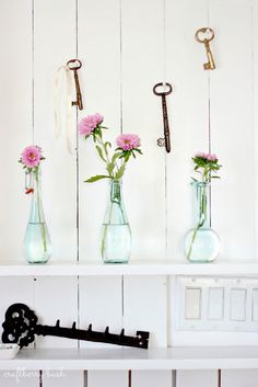 three vases with pink flowers and keys on a shelf above a key holder that is attached to the wall