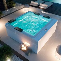 an outdoor hot tub lit up at night with lights on the floor and in between two lounge chairs