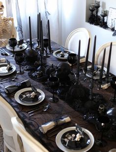 a dining room table set for halloween with black and white plates, silverware and candles