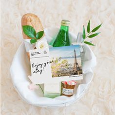 a basket filled with assorted items on top of a white table next to a bottle of wine