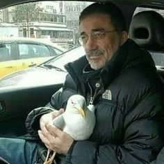 a man sitting in the back seat of a car while holding a white bird on his lap