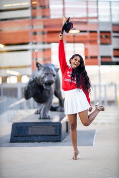 a woman in a red shirt and white skirt is posing next to a statue with her hands up